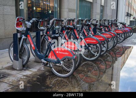 Row of Santander hire bikes on the street with reflections in a large puddle. London