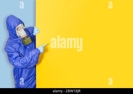 Man in full protective clothing wearing a gas mask demonstrating empty blank place copyspace for sample text on a yellow background. Coronavirus quara Stock Photo