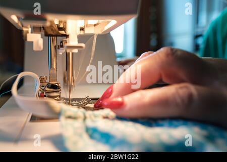 Female hands sew a protective mask using a modern electric sewing machine. Concept of safety during a viral epidemic. Stock Photo