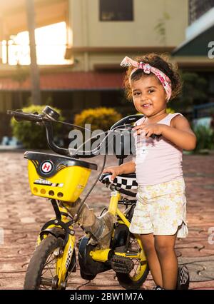 Margao, Goa/India - May 10 2020 : Playful Pretty Indian girl child/infant/toddler wearing a hair band, playing with a cycle/tricycle. Stock Photo