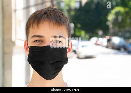 Young man in a black medical protective mask on an empty city street with cars near a park and road. Copyspace. Alone. Smog and dust protection concep Stock Photo