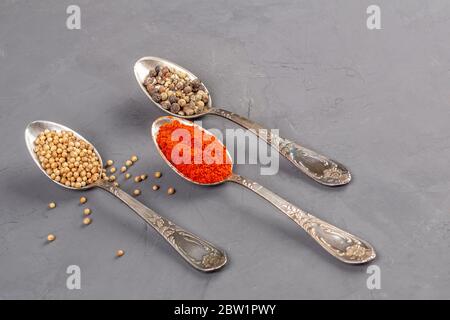 Closeup coriander seeds and ground paprika and black pepper peas in teaspoons Stock Photo
