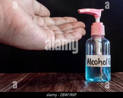 Hand sanitizer Alcohol gel pump with hand on wooden table on dark background. Stock Photo