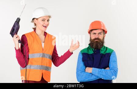 Family making repair, husband annoyed by wife. Builder makes hole in male head. Annoying repair concept. Woman with happy face drills head of man, white background. Man with pensive face in helmet. Stock Photo