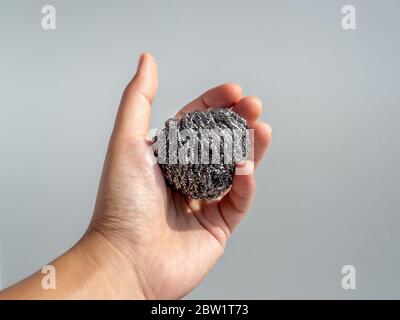 Hand holding steel wool scrubbing pots. Stainless steel sponge in hand isolated on white background. Stock Photo