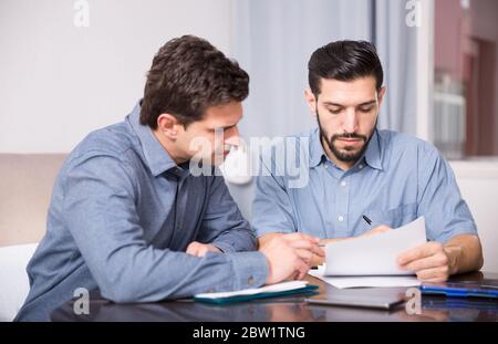 Two young men in serious discussion at home table while analysing documents together Stock Photo
