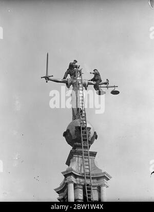 Balanced in the scales of justice. Clambering over the outstretched arms of justice and standing nonchalantly in her very scales, workmen are re-gilding for the Coronation the famous statue which surmounts the Old Bailey. Photo shows: a workman as they re-gild the figure of Justice high over the Old Bailey. 19 April 1937 Stock Photo