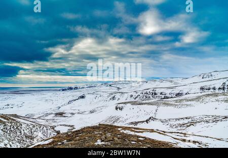 Dramatic clouds over snow covered mountain landscape with road in the background Stock Photo