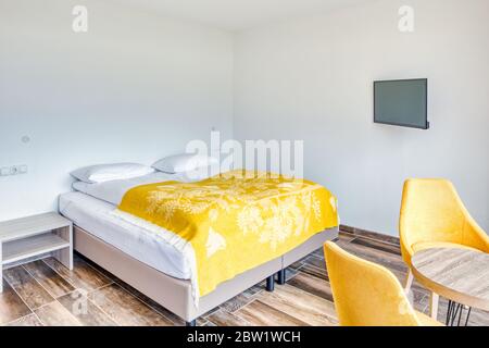 Modern minimalist hotel room with yellow wool chairs and blanket. Wooden tile floor. Plain white wall without decoration. Tv on the wall Stock Photo