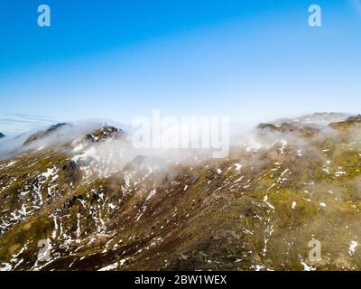 Drone photo of the top of a mountain chain covered in clouds and illuminated by the morning sun Stock Photo