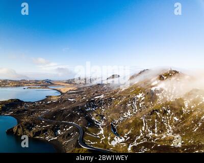 Cloud covered mountain peaks next to a lake with a small road passing through the mountains Stock Photo