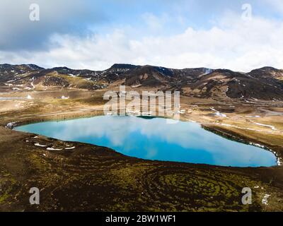 Green small lake reflecting the clouds, surrounded by mountains Stock Photo