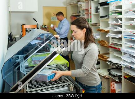 Female worker packs notebooks in a vacuum packing Stock Photo