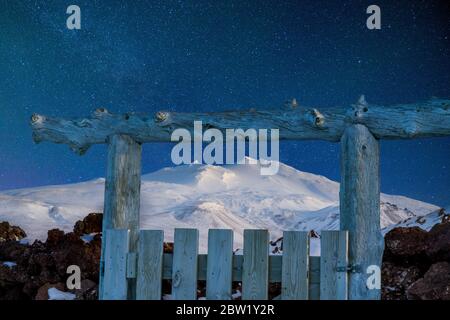 Wooden fence in front of snowy glacier mountain with starry sky in the background Stock Photo