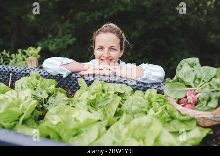 beautiful woman posing next to raised garden bed and her fresh vegetables Stock Photo