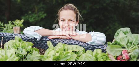 beautiful woman posing next to raised garden bed and her fresh vegetables Stock Photo