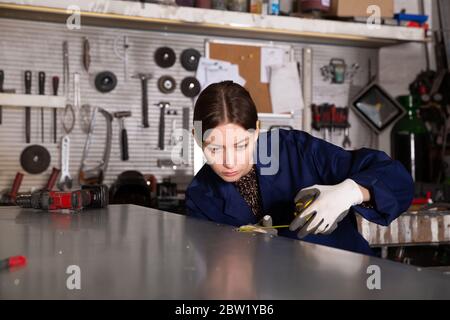 Skilled young craftswoman working in industrial workshop, measuring metal structures Stock Photo