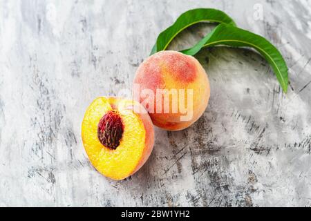 Peach and half peach with leaf on gray concrete background. Fresh sweet peach with pitted. Top view fresh organic peach fruit Stock Photo