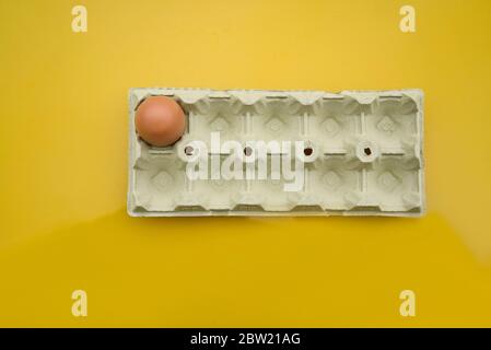 Lone egg in its horizontal carton of a dozen eggs. Yellow background yolk color. Brown egg. Photo zenital Stock Photo