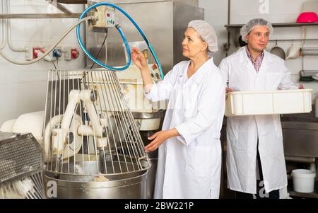 Nice bakers controlling process of making bread dough in kneading machine in bakery Stock Photo