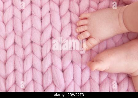 Tender children's legs on a knitted blanket with large loops. Greeting card for baby shower, childbirth, pregnancy. Copyspace. Stock Photo