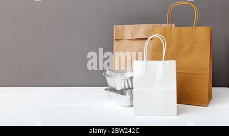 White craft paper bags and food containers on white table gray background. Food delivery service. Takeaway food in foil containers, Empty cardboard Stock Photo