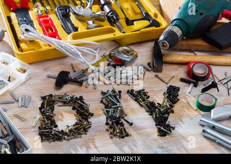 Word DIY lined with metal screws among assorted fasteners, supplies and hand tools on wooden table Stock Photo