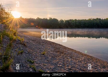 Small local recreation swimming lake in Bavaria, Germany in early morning light with fog over water Stock Photo