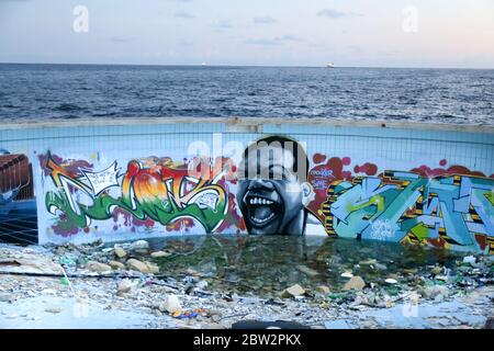 Marsaskala / Malta - Graffiti an african man on the exterior wall of the abandoned swimmingpool in the Jerma Palace Hotel and the view of the sea Stock Photo