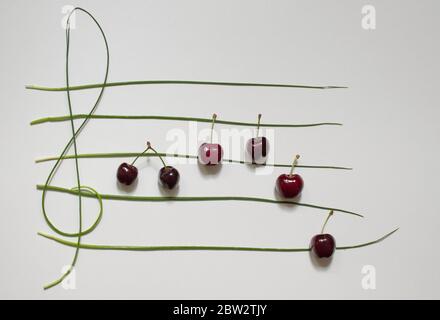 Concept photo of musical staff with cherries and herbs on white background Stock Photo
