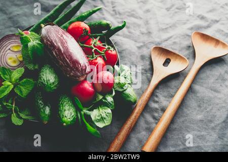 Different fresh colorful vegetables in a plate with wooden kitchen utensils on a table Stock Photo