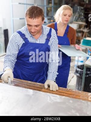Focused male worker with female apprentice working on glass washing machine in workshop Stock Photo
