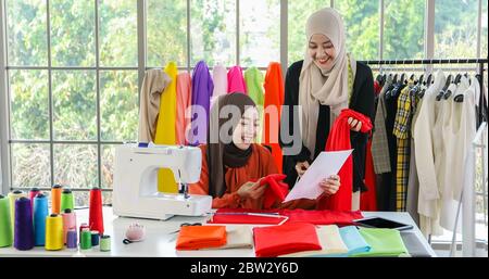 Small business of Muslim woman fashion designer Working and  using smart phone and tablet With Dresses at clothing store Stock Photo