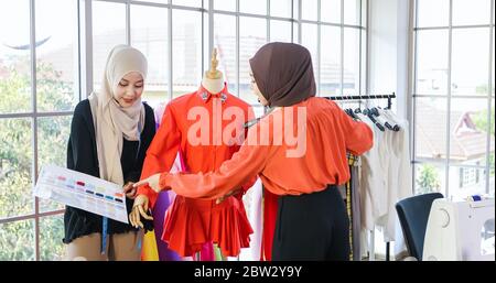 Small business of Muslim woman fashion designer Working and  using smart phone and tablet With Dresses at clothing store Stock Photo