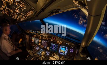 Pilot at work inside modern jet passenger airliner flight deck. Beautiful view from the cockpit, flight and navigation instrument lights dimmed and na Stock Photo