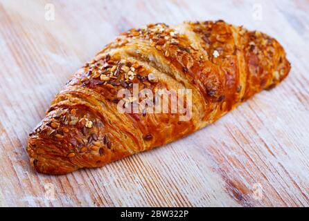 One multigrain croissant sprinkled with seeds of brown and gold flax on wooden background Stock Photo