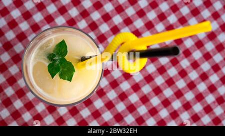 A glass of lemonade with two straws on a checkered red-and-white tablecloth. Stock Photo