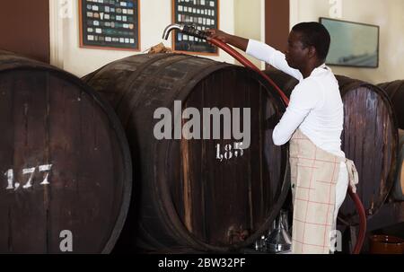 Confident male winemaker working in wine cellar, filtering wine in barrels Stock Photo
