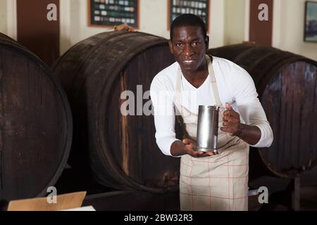 Smiling African American male vintner proposing degustation of wine in modern wine shop Stock Photo