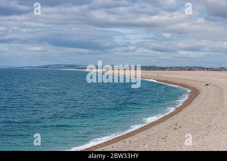 View of the beautiful Chesil beach on a warm summer morning with several people in the distance enjoying the sunny weather Stock Photo