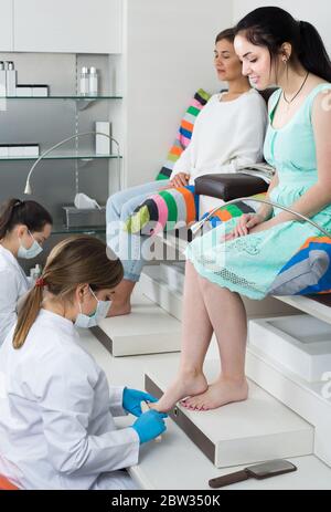 Pair of happy spanish women clients getting pedicure in modern nail salon Stock Photo