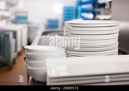 Closeup of clean white plates stacked on table in restaurant kitchen Stock Photo