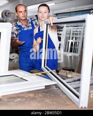Positive man and woman in blue overalls assembling pvc windows at factory Stock Photo