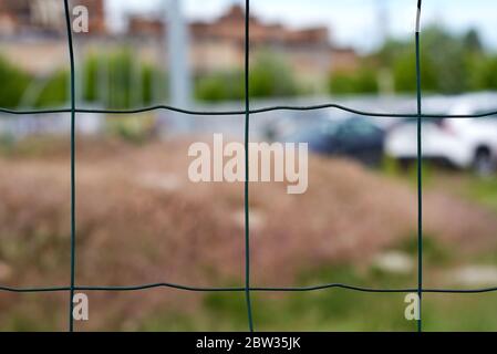 large metal green mesh fence, blurred cityscape, close up Stock Photo