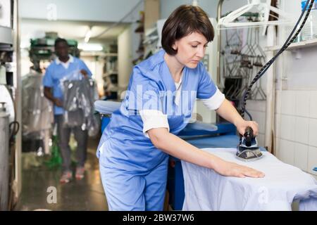 Young female laundry worker ironing clean clothes in dry cleaning salon Stock Photo