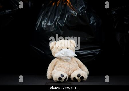 A teddy bear in a gauze medical bandage sits on the background of large garbage bags Stock Photo