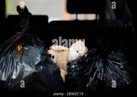 A teddy bear in a protective medical bandage lies on garbage bags in the trunk of a car Stock Photo