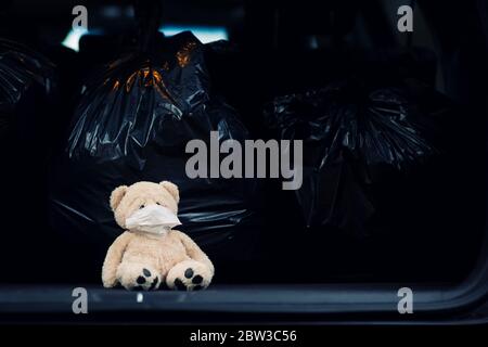 a teddy bear in a medical mask sits in the trunk of a car with garbage bags Stock Photo