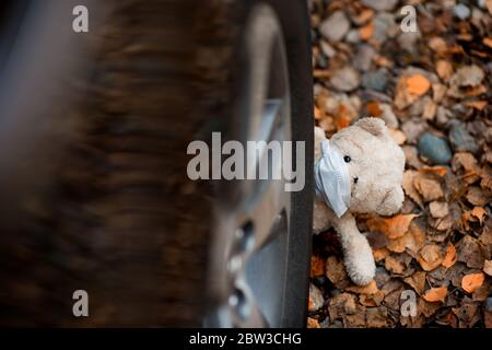 a teddy bear in a medical mask sadly looks out from under the wheel of the car Stock Photo