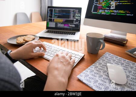 Close-up of unrecognizable programmer sitting at desk with coffee and cookies and creating code for computer software Stock Photo